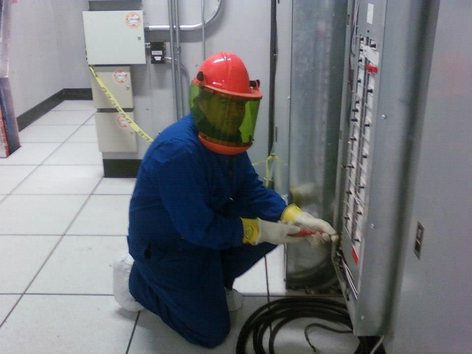 Un travailleur en équipement de protection agenouillé près d'un panneau électrique.