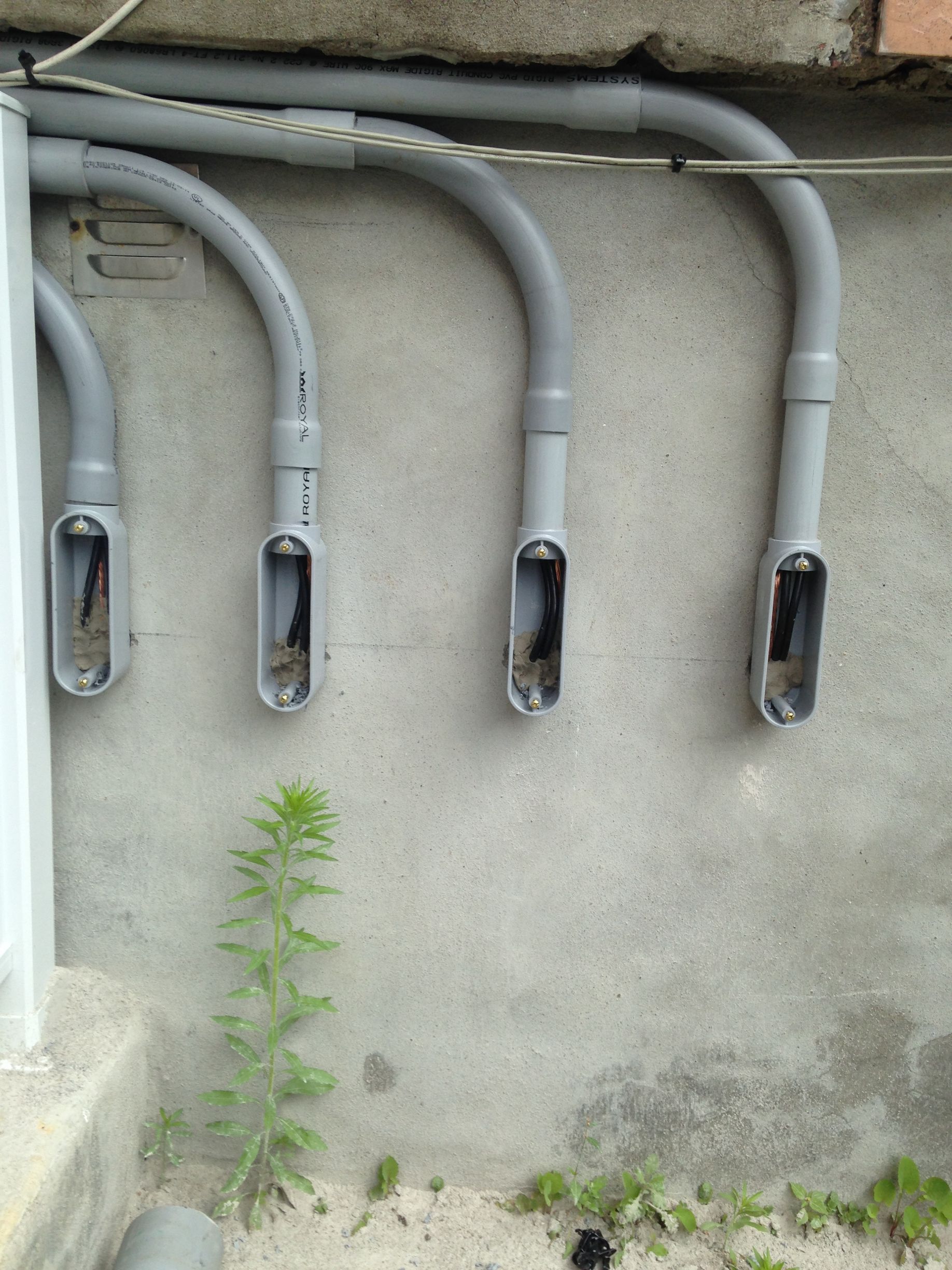 Conduits électriques gris à extrémités ouvertes, fixés à un mur en béton.