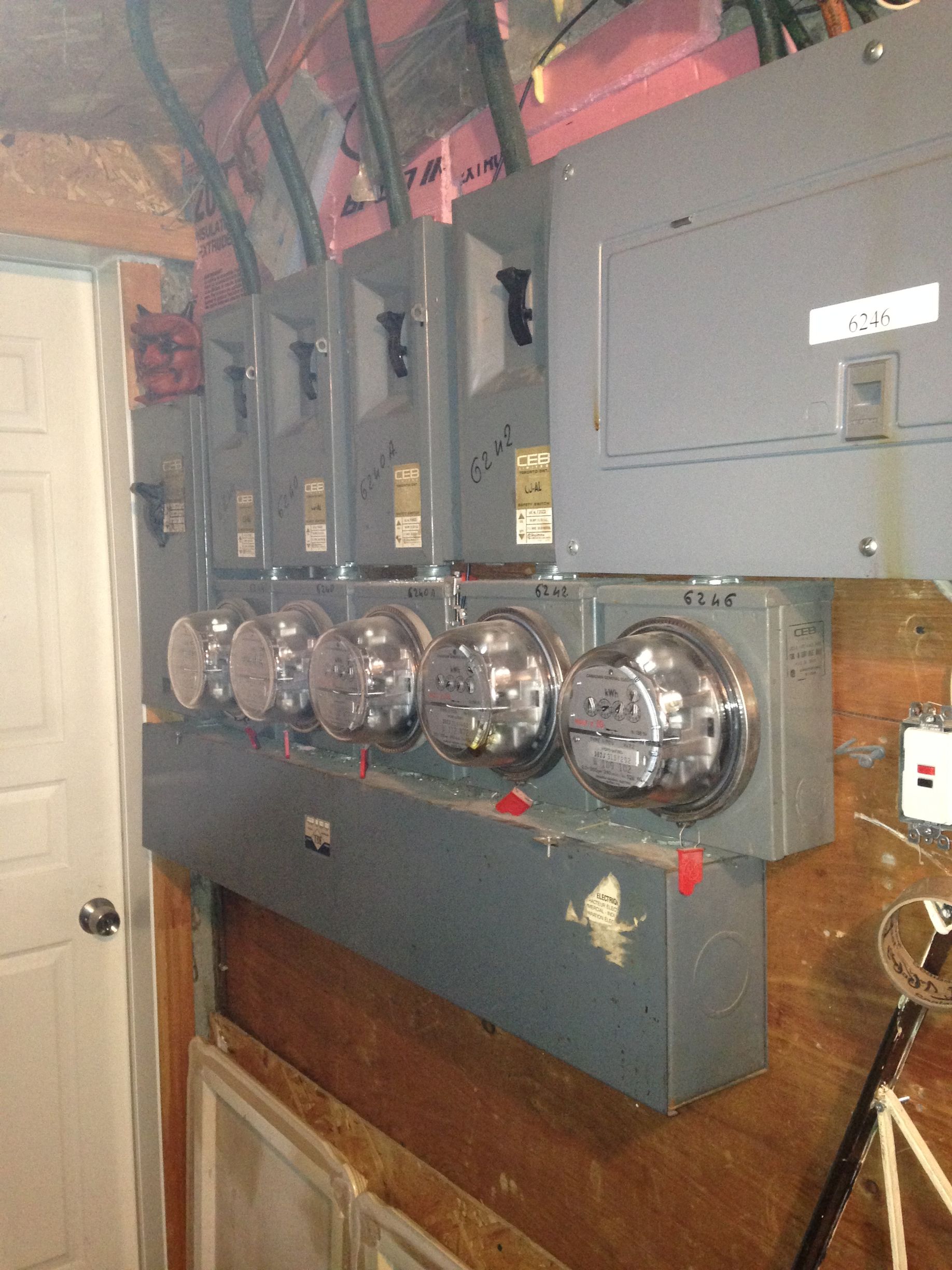 Panneau de compteurs électriques avec plusieurs compteurs et disjoncteurs, probablement pour un logement à plusieurs unités.