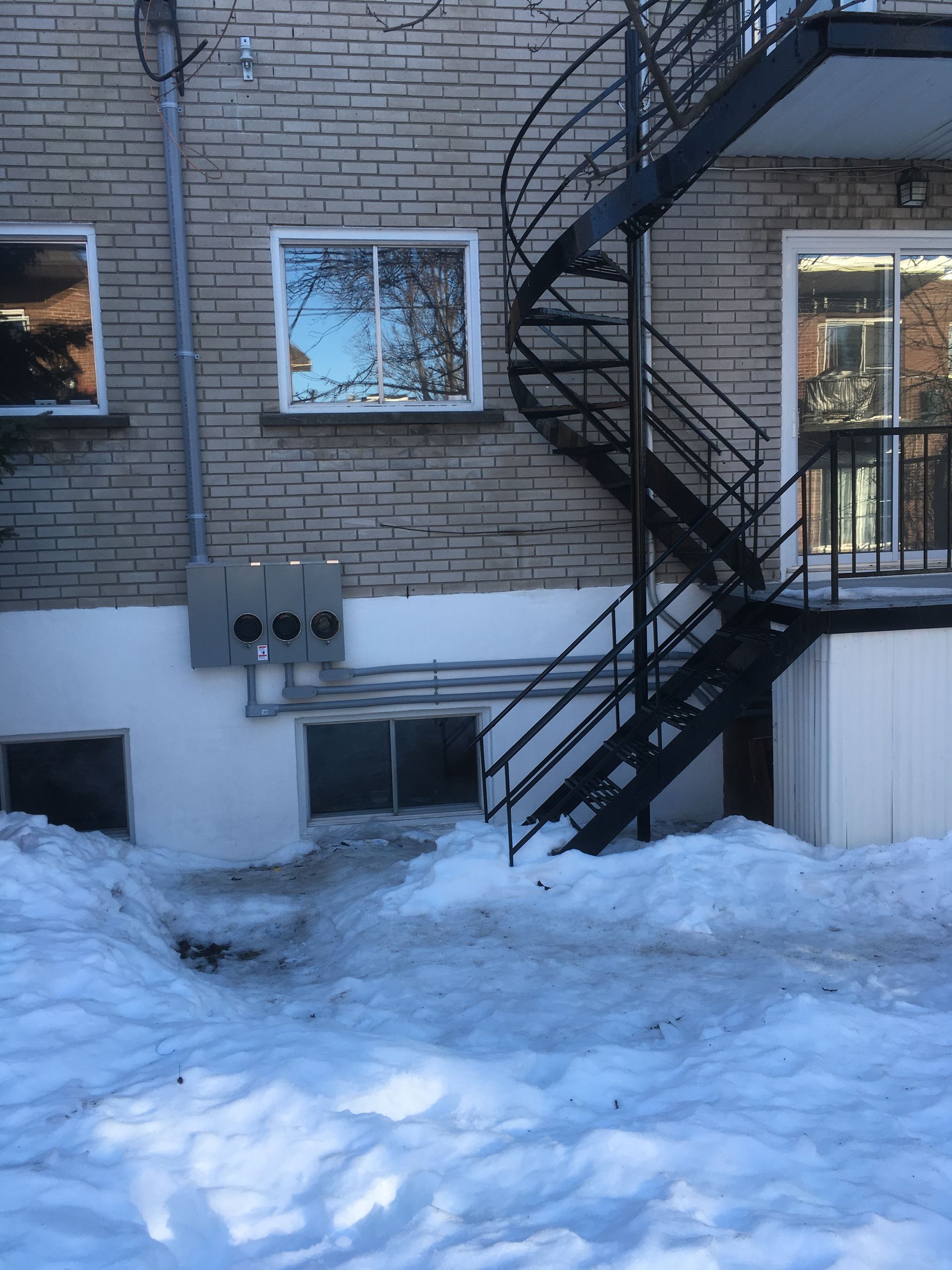 Arrière extérieur du bâtiment avec mur de briques, escalier en colimaçon, neige au sol.