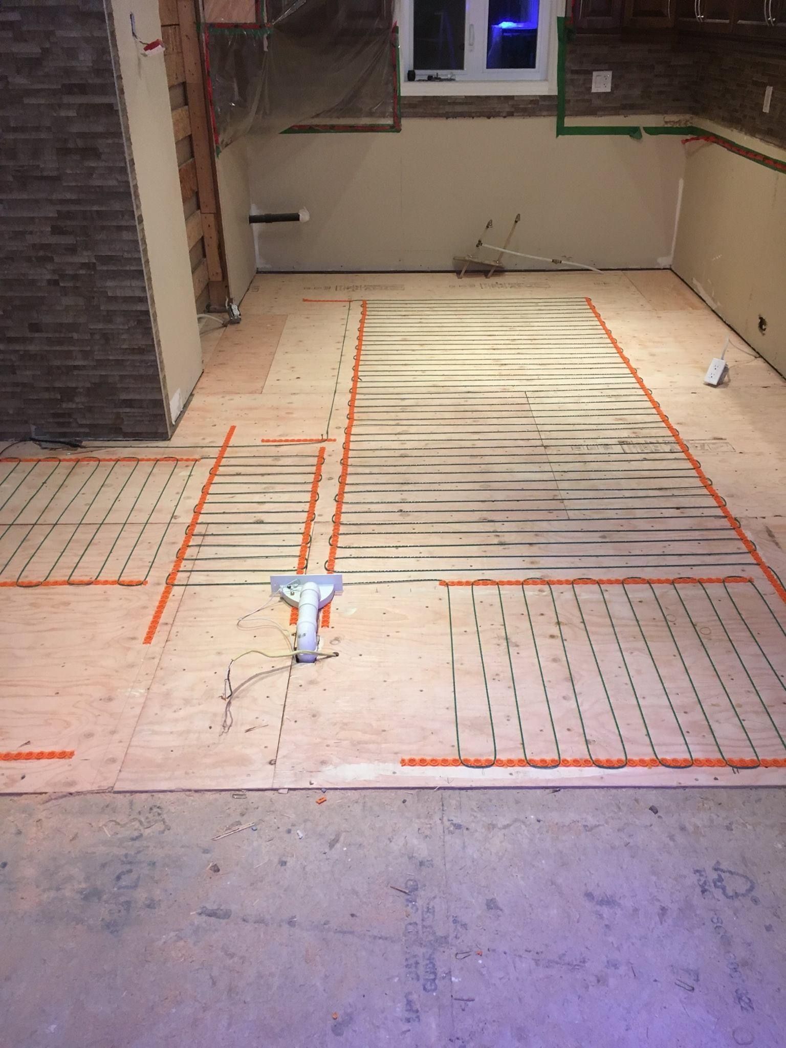 Installation d'un système de chauffage par le sol. Fils chauffants orange sur un sous-plancher en bois, contre un mur en pierre, près d'une fenêtre.