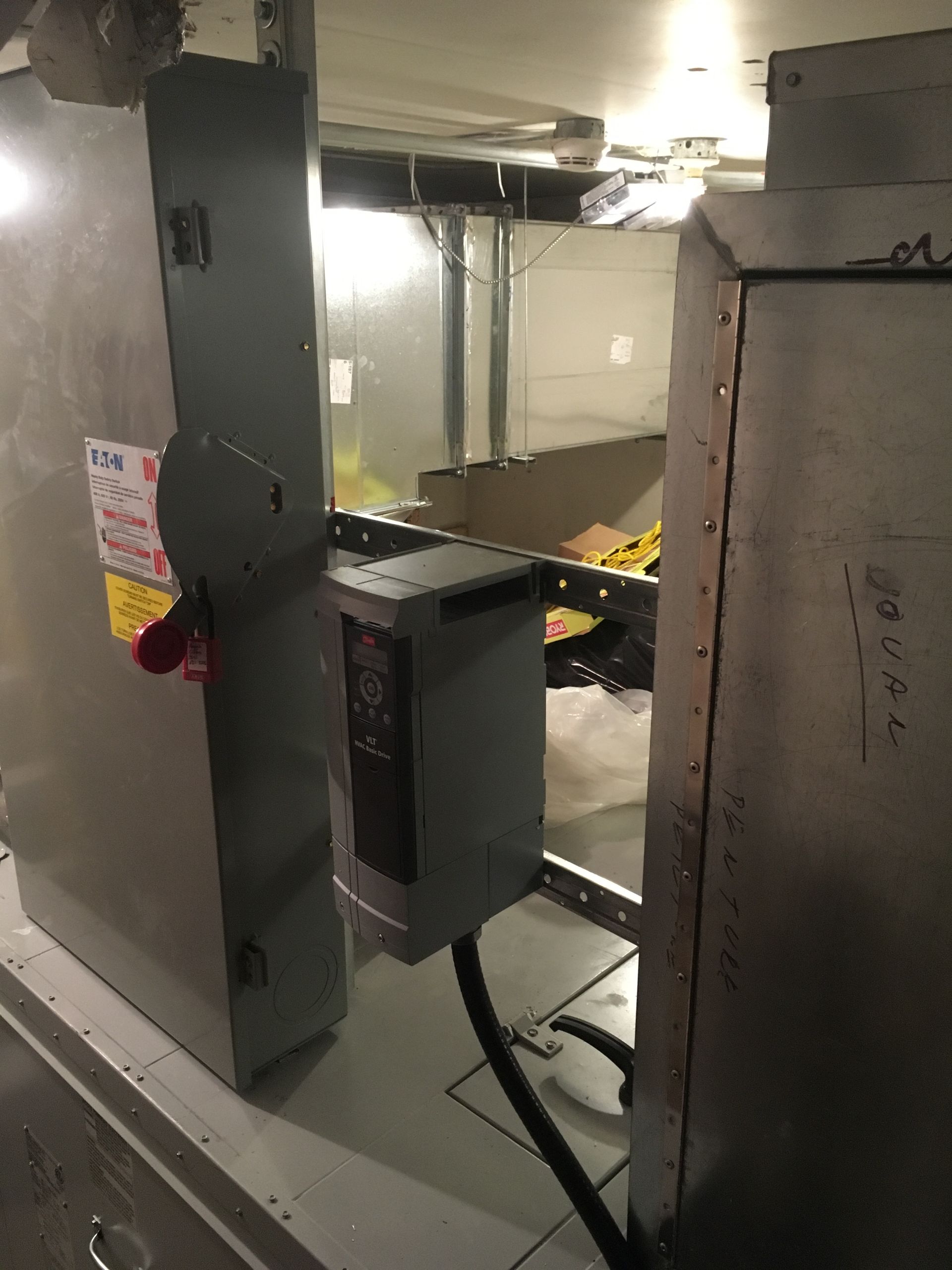 Panneau électrique gris et unité VFD, installés à proximité de conduits dans un environnement industriel.