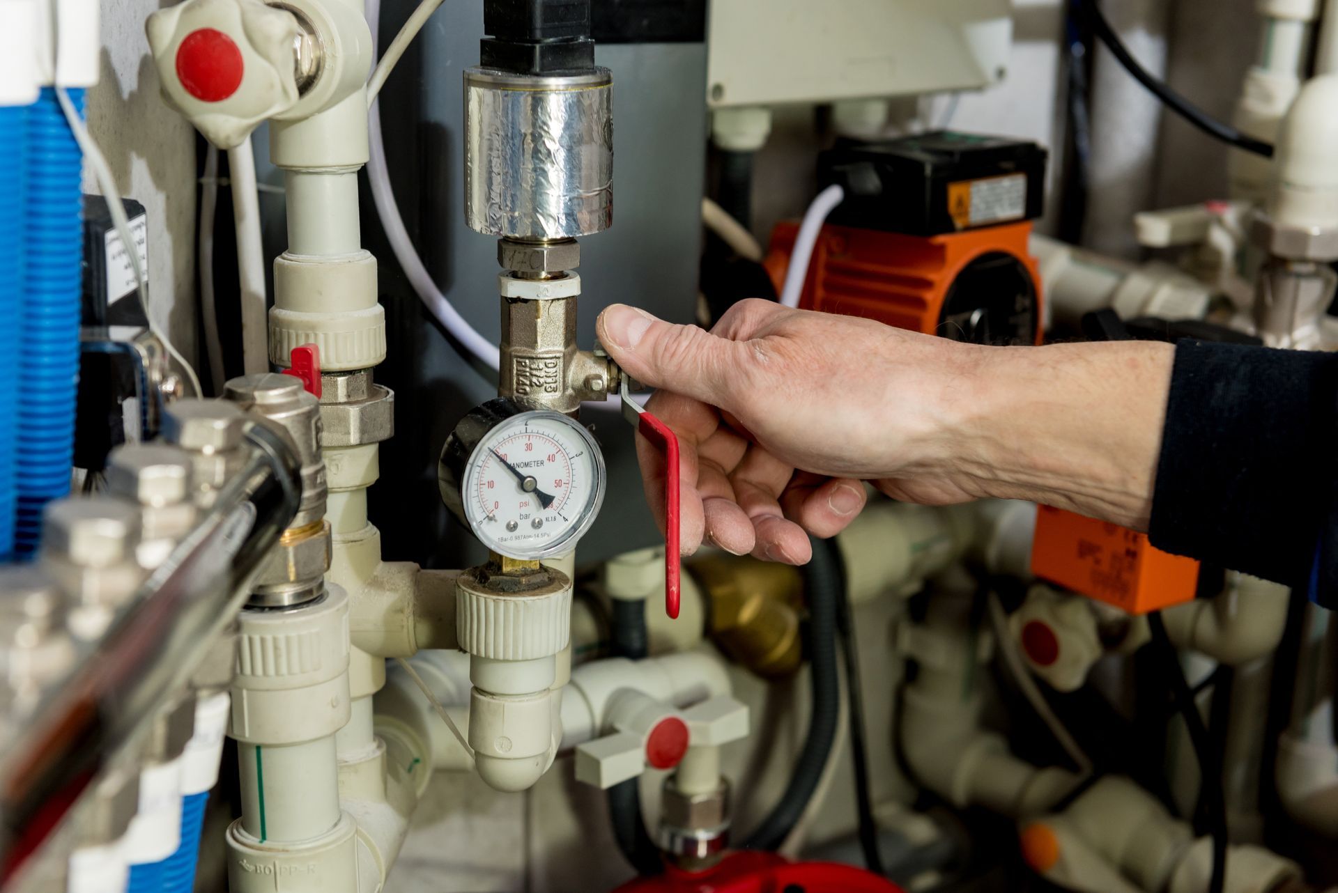 A person’s hand adjusting a red-handled valve on a plumbing system with a pressure gauge.