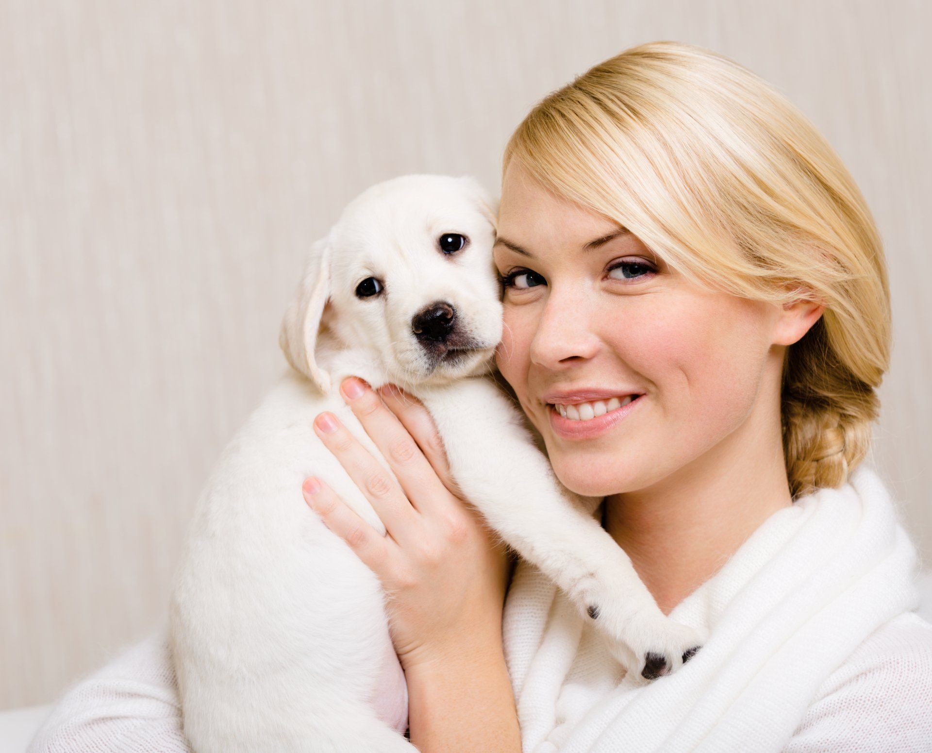 A woman is holding a white puppy in her arms and smiling.