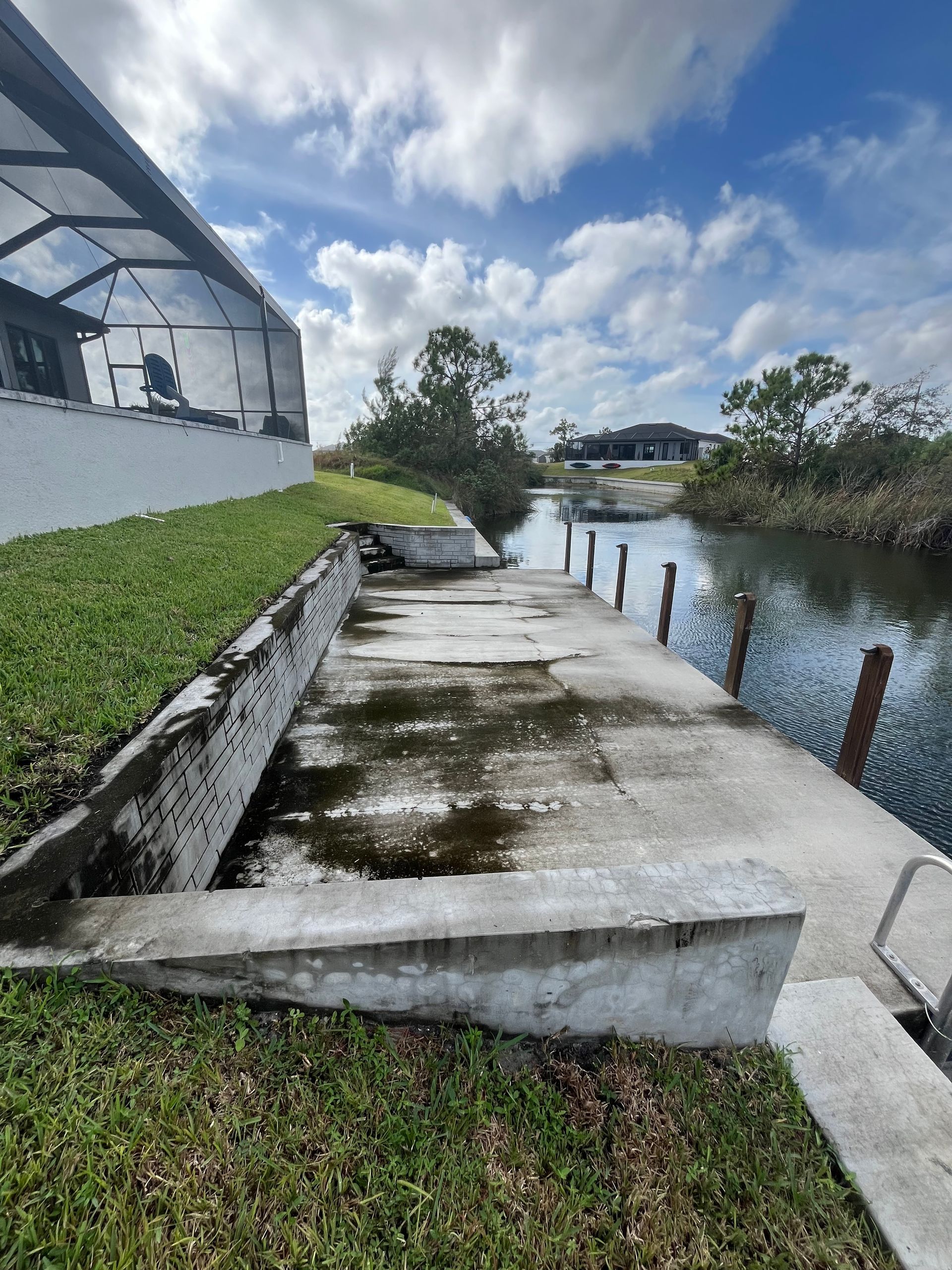 A concrete walkway leading to a body of water next to a house.