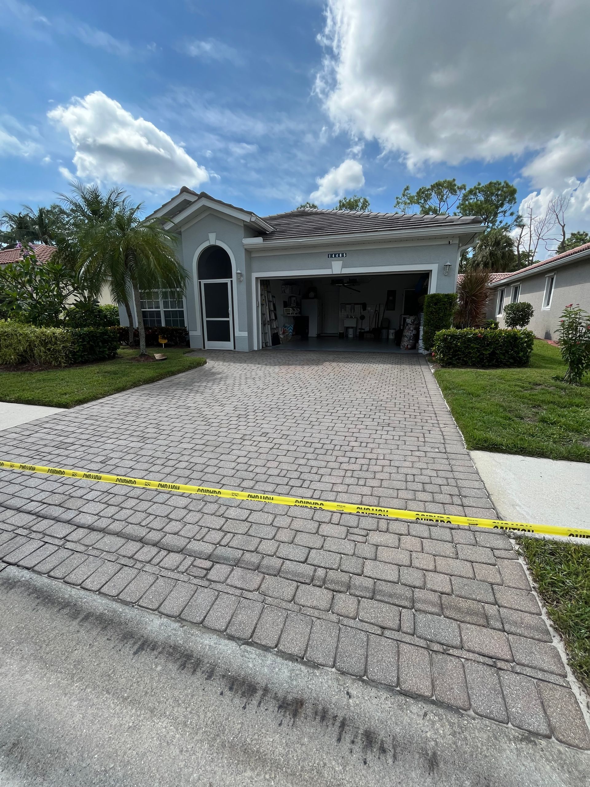 A house with a brick driveway and a garage is surrounded by yellow tape.