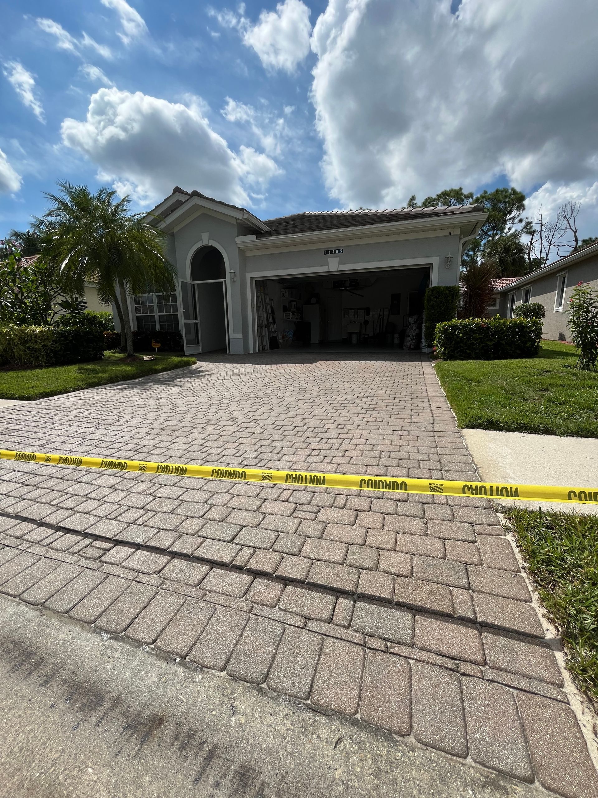 A house with a brick driveway is surrounded by yellow tape.