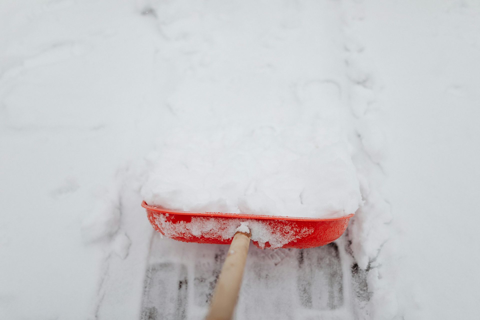 A red snow shovel is being used to remove snow from the ground.