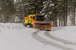 A snow plow is driving down a snow covered road.