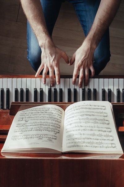 A pianist wearing blue jeans sits at a piano and plays while reading musical notes on paper