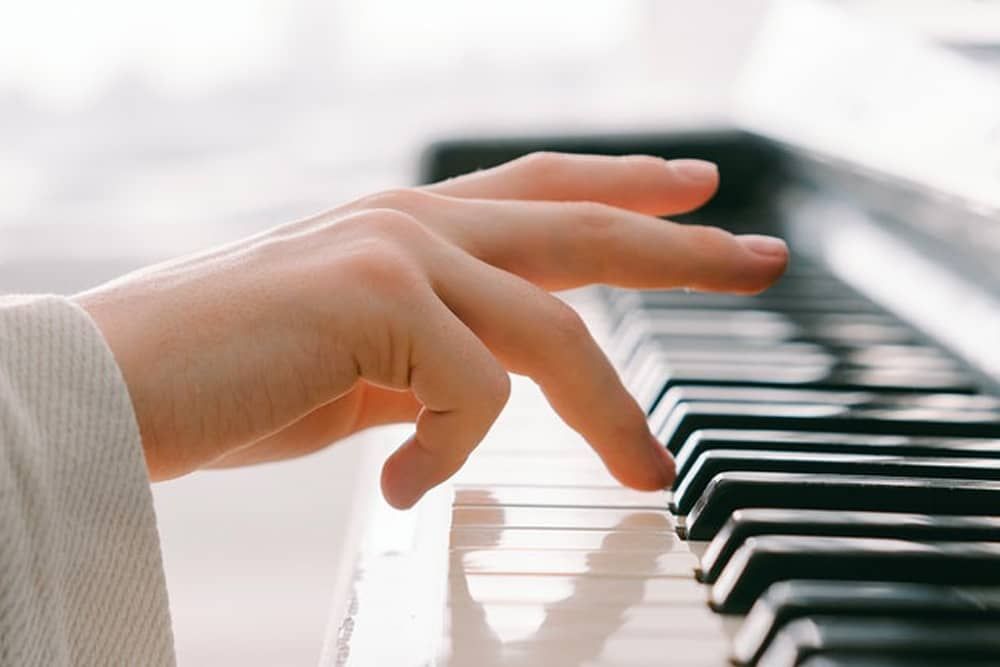 Music Lessons: A person is playing a piano with their fingers on the keys.