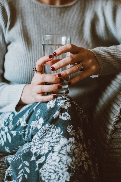 A vocal student sits on a sofa and stays hydrated with a glass of water