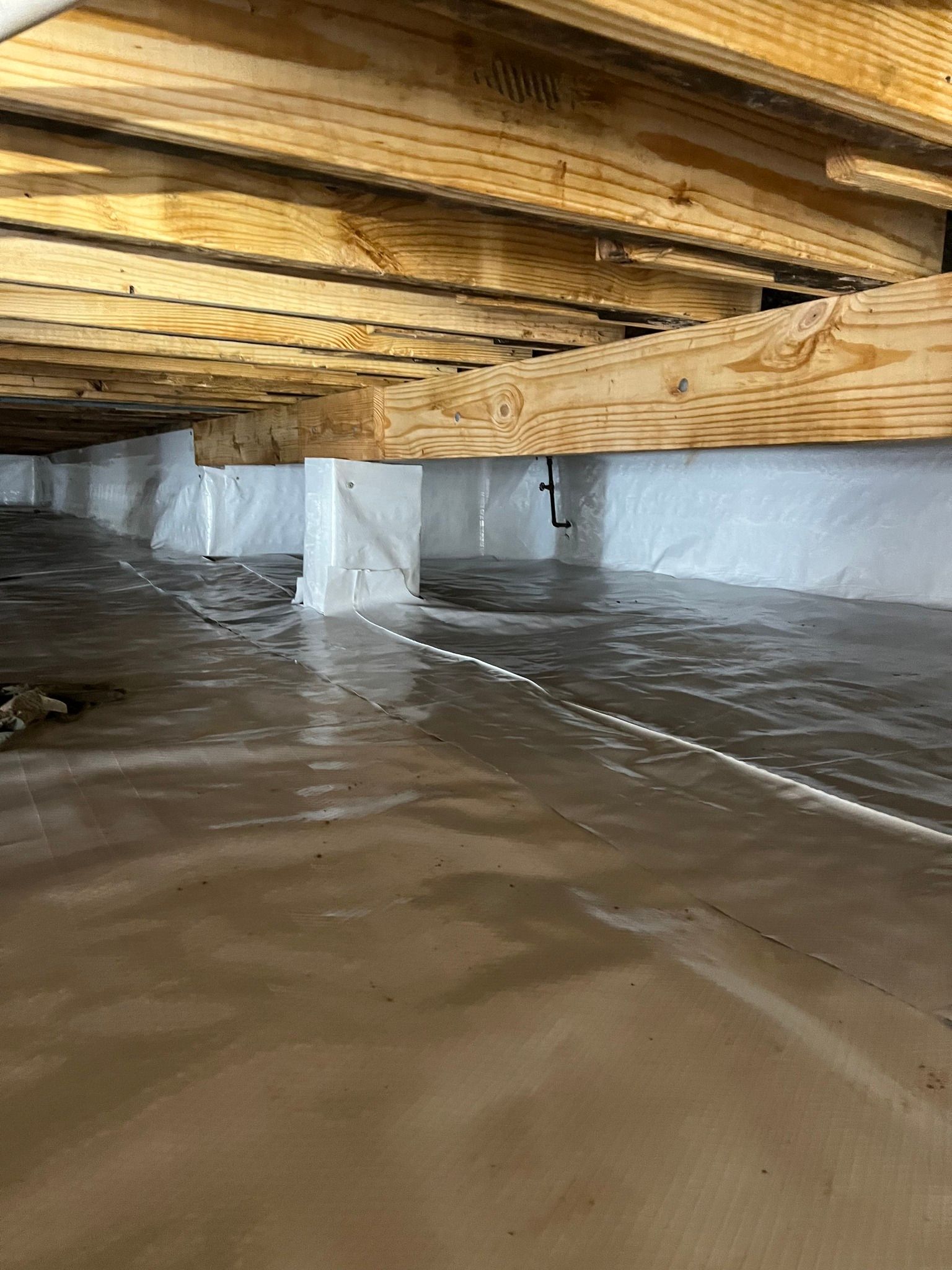 A flooded basement with wooden beams and plastic covering.