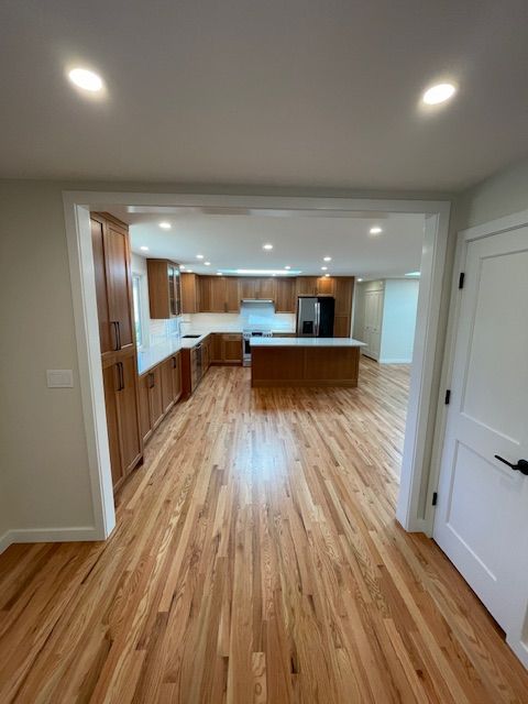 Bright empty kitchen and living area with hardwood floors, white walls, and recessed lighting