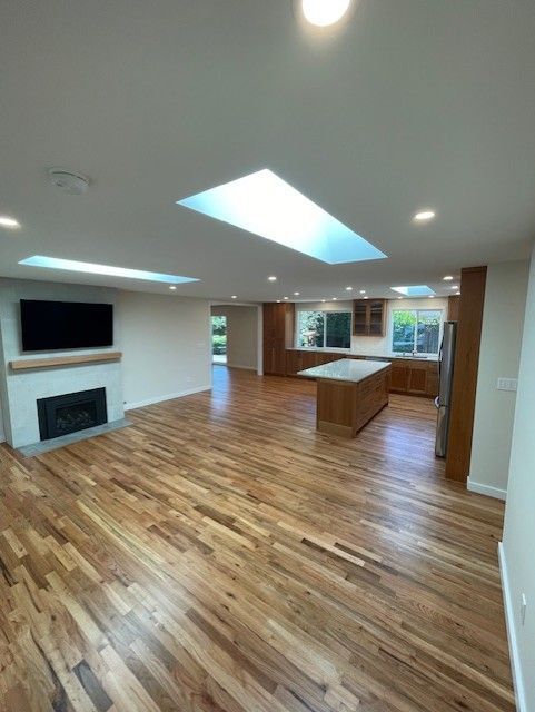 Bright open kitchen and living room with wood floors, skylights, fireplace, and island