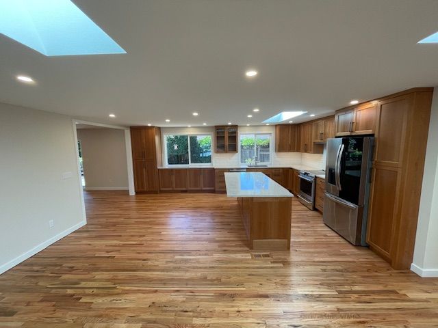 Bright modern kitchen with wood floors, large island, skylights, and stainless steel appliances