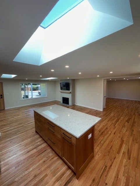Empty modern kitchen and living area with wood floors, skylights, island, and recessed lighting