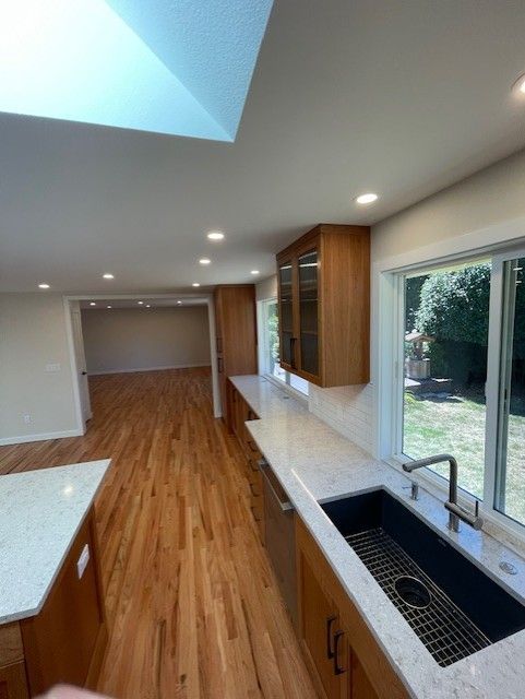 Modern kitchen with wood floors, white countertops, sink, and large windows opening to a backyard.