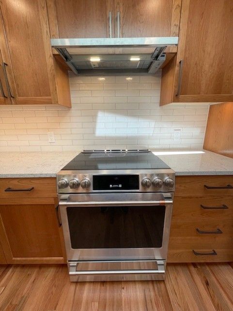 Stainless steel stove and oven centered between wood cabinets in a kitchen with white tile backsplash.