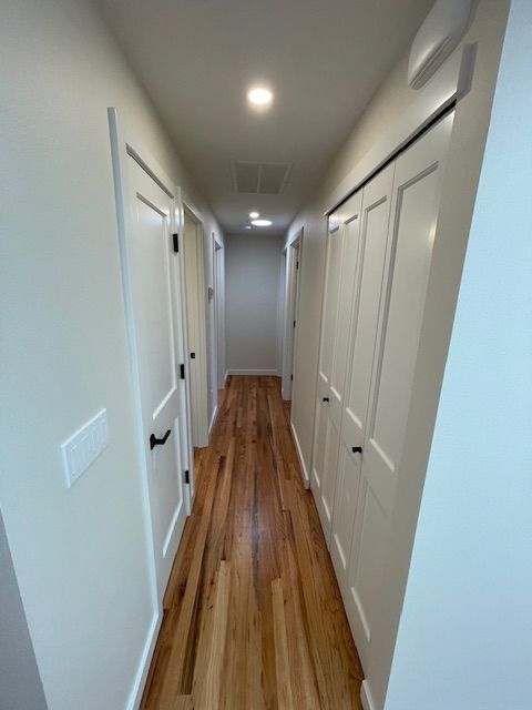 Narrow hallway with white doors and wood floor, lit by recessed ceiling lights.