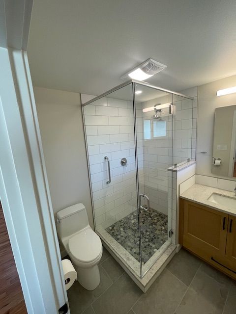 Modern bathroom with glass shower, toilet, and wood vanity with sink