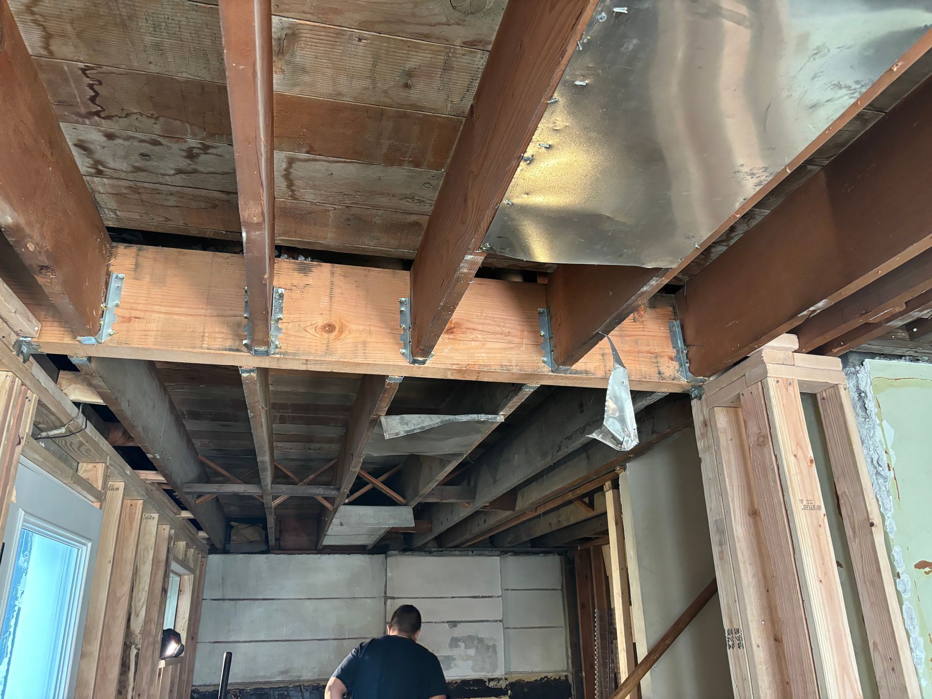 Unfinished basement with exposed ceiling beams, insulation, and a person standing near the back wall.