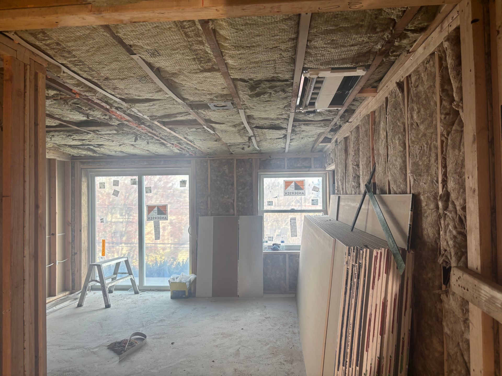 Unfinished room with exposed insulation, windows, and construction materials on the floor and right wall.