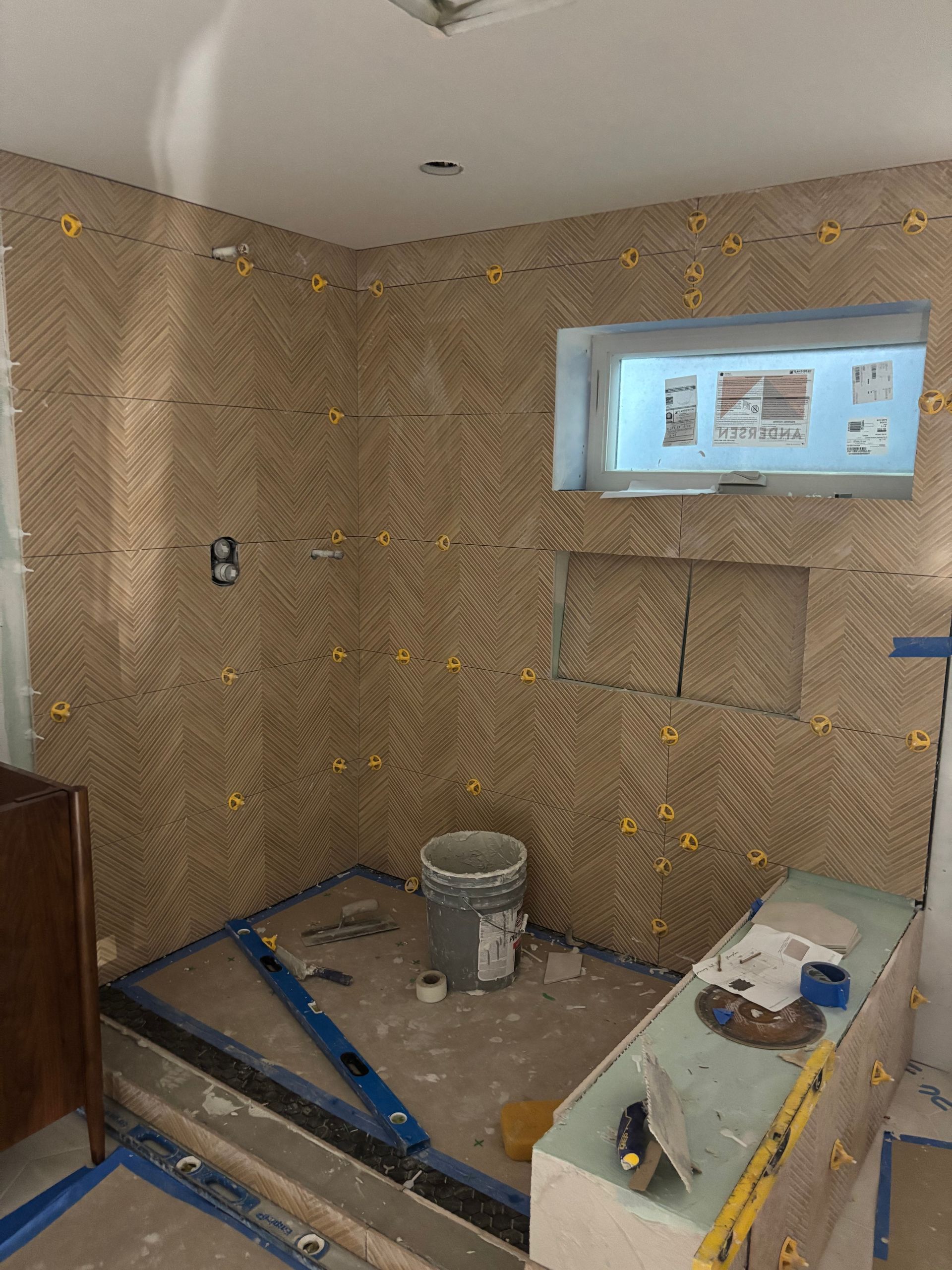 Partially tiled bathroom under renovation with tools, bucket, and a wall-mounted monitor display.