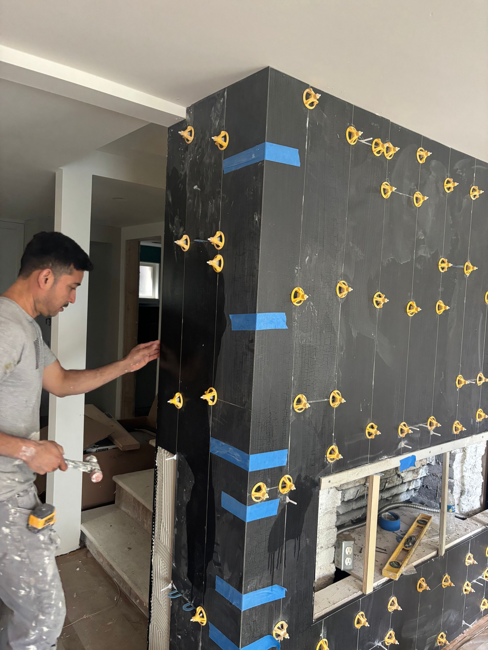 Worker installing black wall panels with blue tape on a construction site