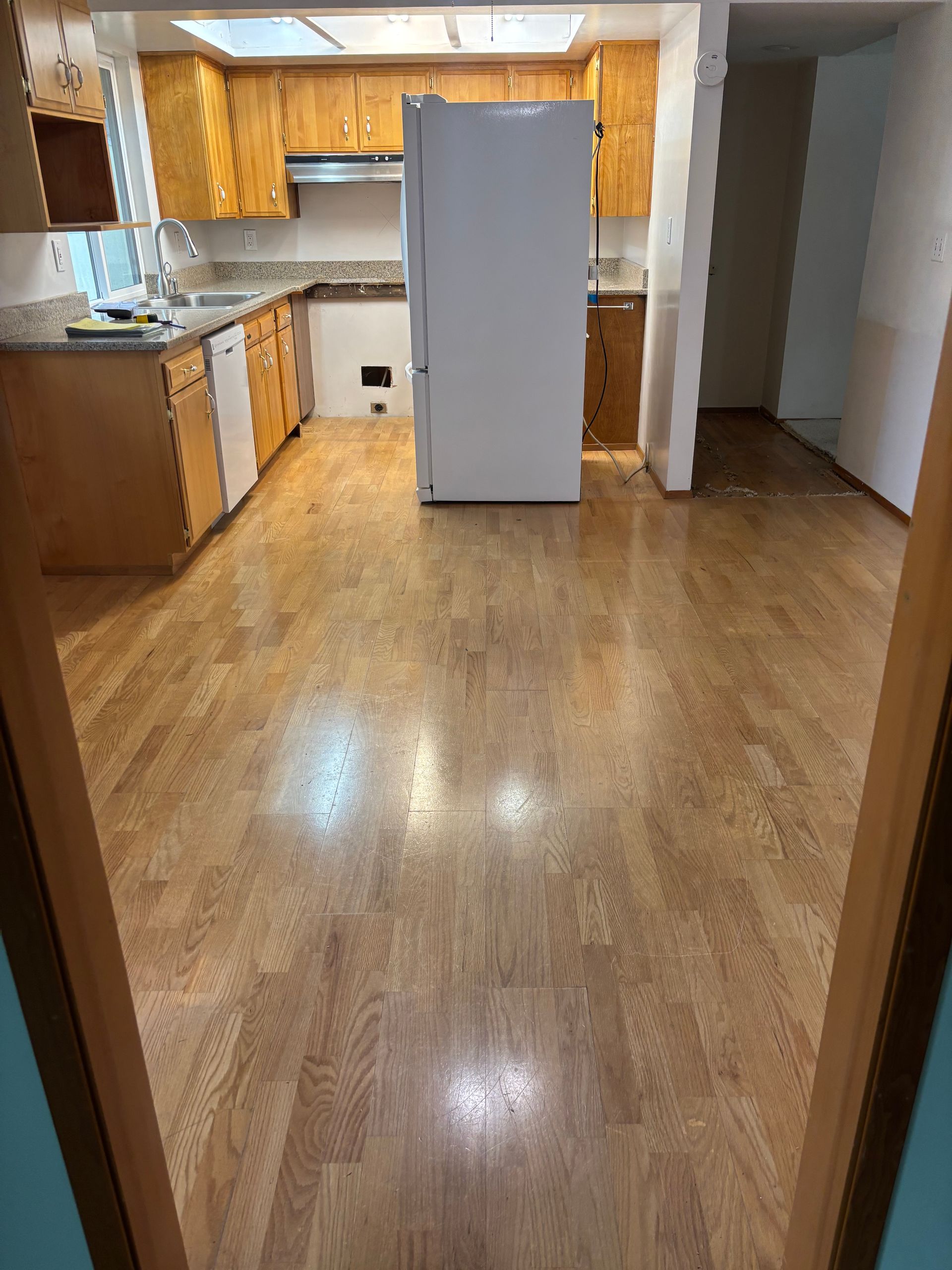Empty kitchen with wood floors, white refrigerator, and wooden cabinets, viewed from a doorway