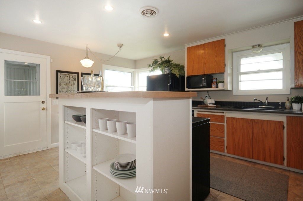 Bright kitchen with white island shelves, wood cabinets, black countertops, and a window over the sink