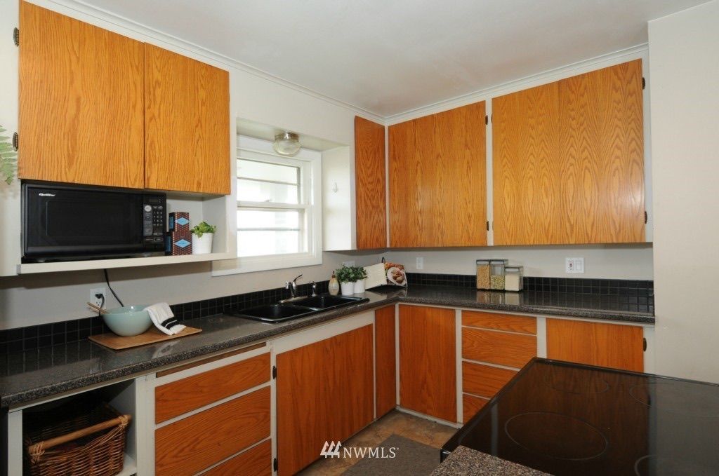 Small kitchen with wood cabinets, black countertops, stove, microwave, and a window.