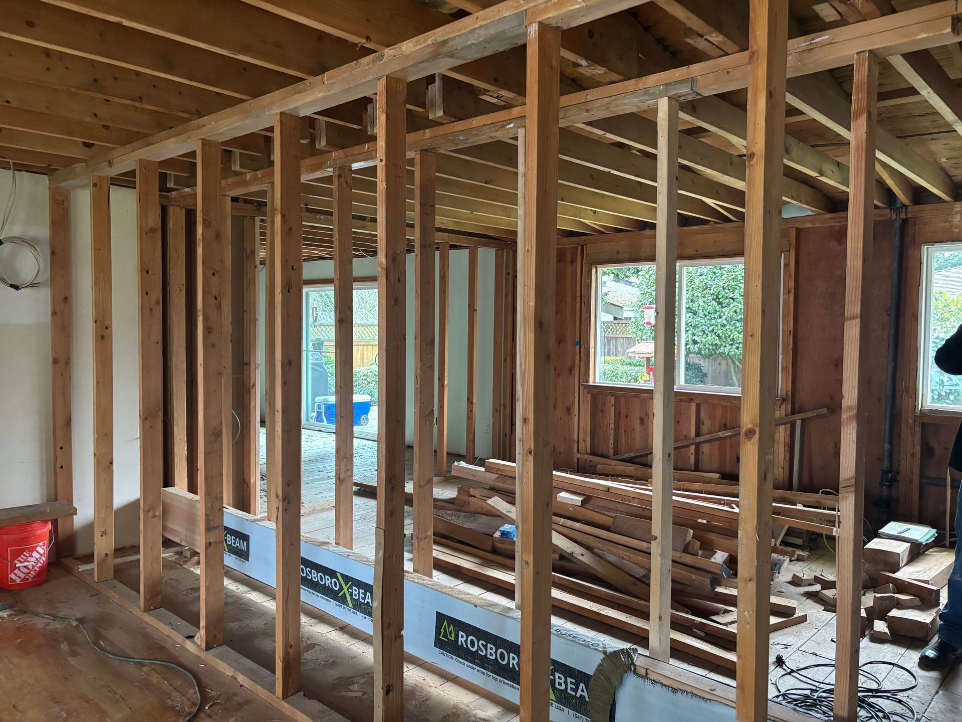 Interior construction framing of a room with exposed wooden studs, beams, and open windows.