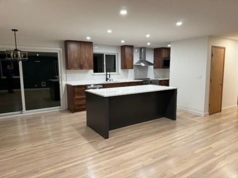 Modern empty kitchen with dark island, white countertops, wood cabinets, and sliding glass doors