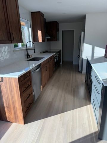 Modern kitchen with wood cabinets, white countertops, and sunlight streaming onto the floor.