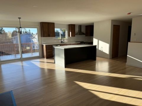 Empty modern kitchen and living room with wood floors, island, and sunlight streaming through sliding glass doors