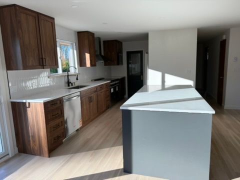 Modern kitchen with dark wood cabinets, white countertops, and a large island in a bright room.