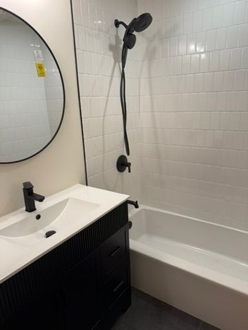 Small modern bathroom with sink, round mirror, showerhead, and bathtub with white tile walls