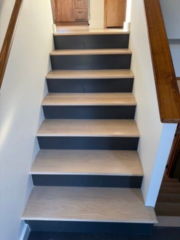 Indoor staircase with dark treads, light wood edges, and wooden railings leading to a doorway