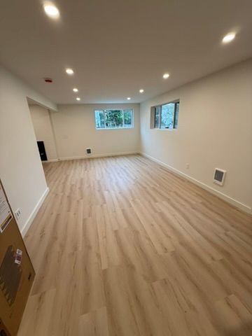 Empty modern room with light wood flooring, recessed lights, and two windows.