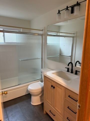 Modern bathroom with glass shower, toilet, and wood vanity with black fixtures