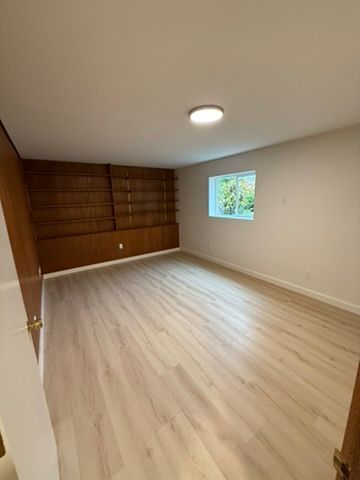 Empty beige room with light wood flooring, built-in wood shelving, and a small window.