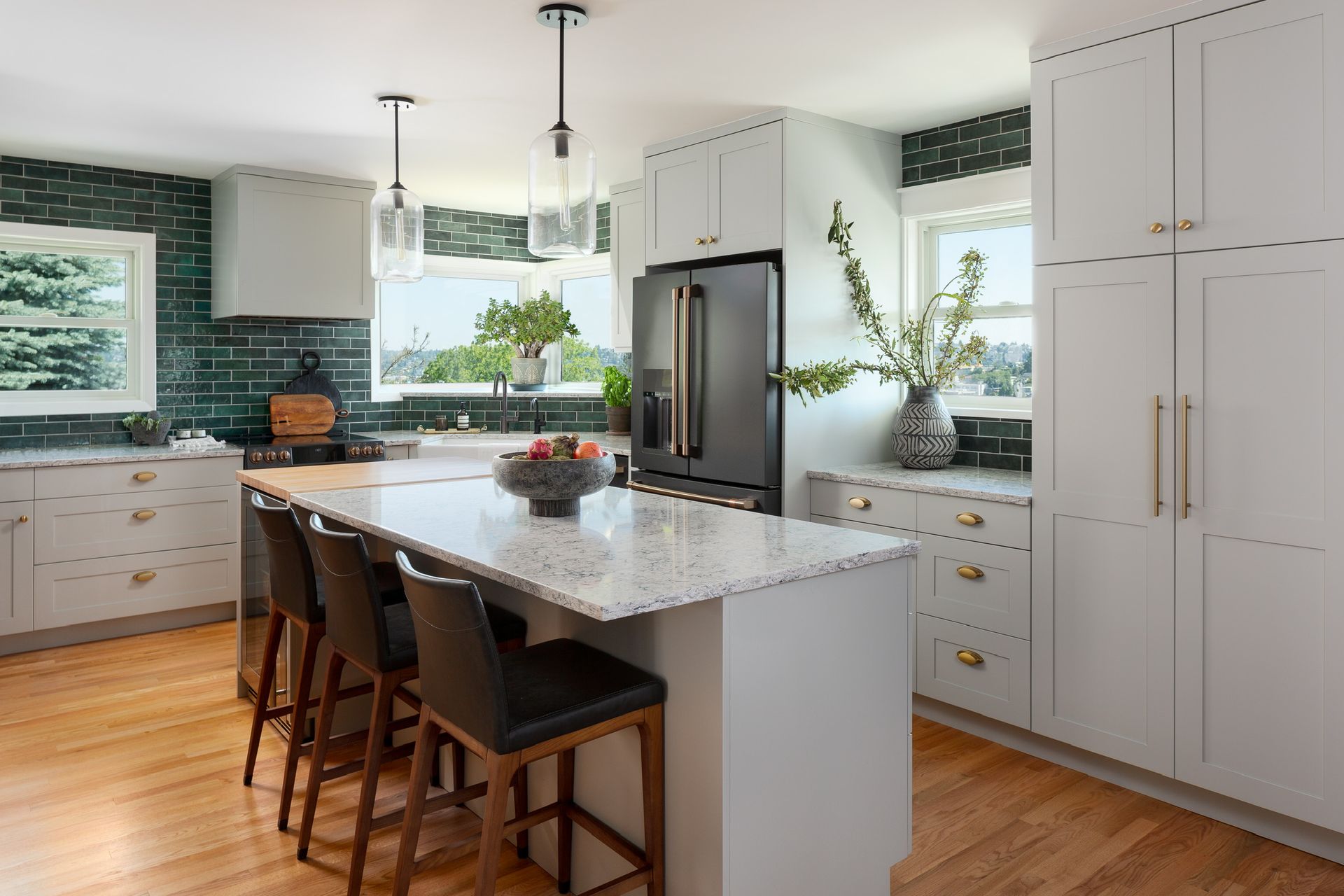 Bright modern kitchen with white cabinets, marble island, wood floors, and black stools by large windows