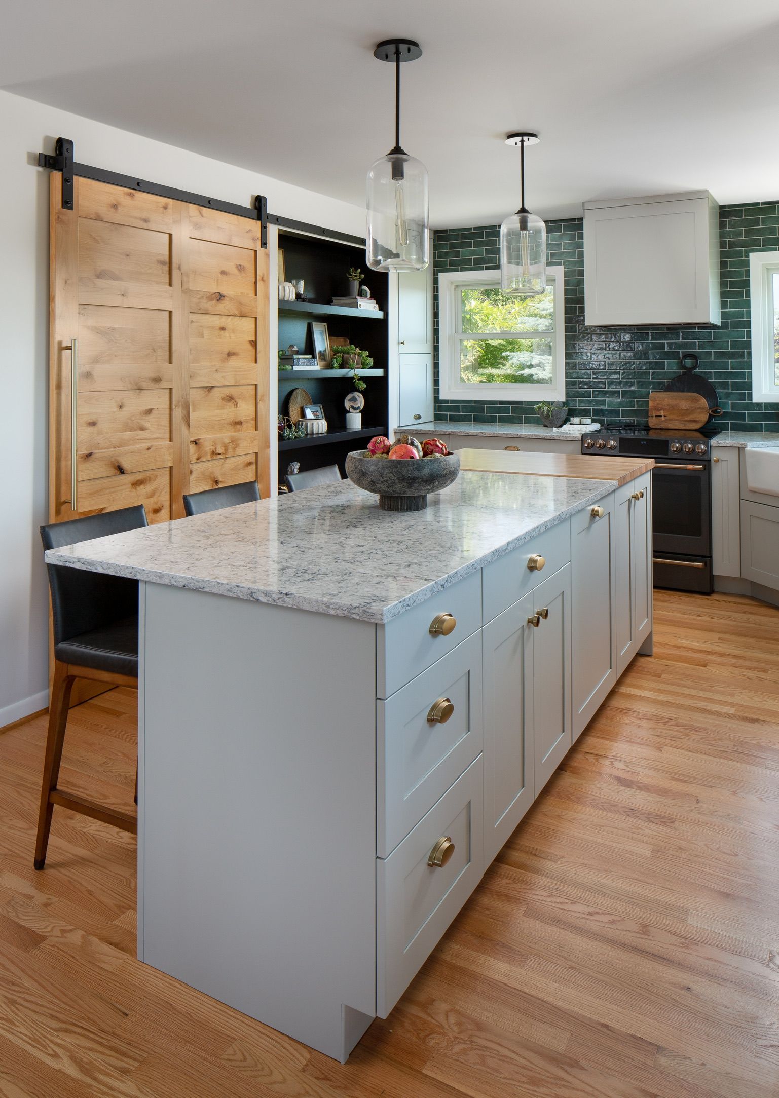 Modern kitchen with gray island, barn-style door, black accents, and large windowed backsplash