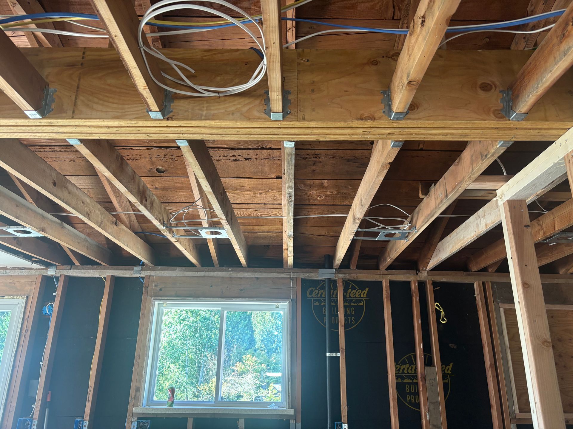 Unfinished room with exposed wooden ceiling joists, framing, and a window letting in daylight.