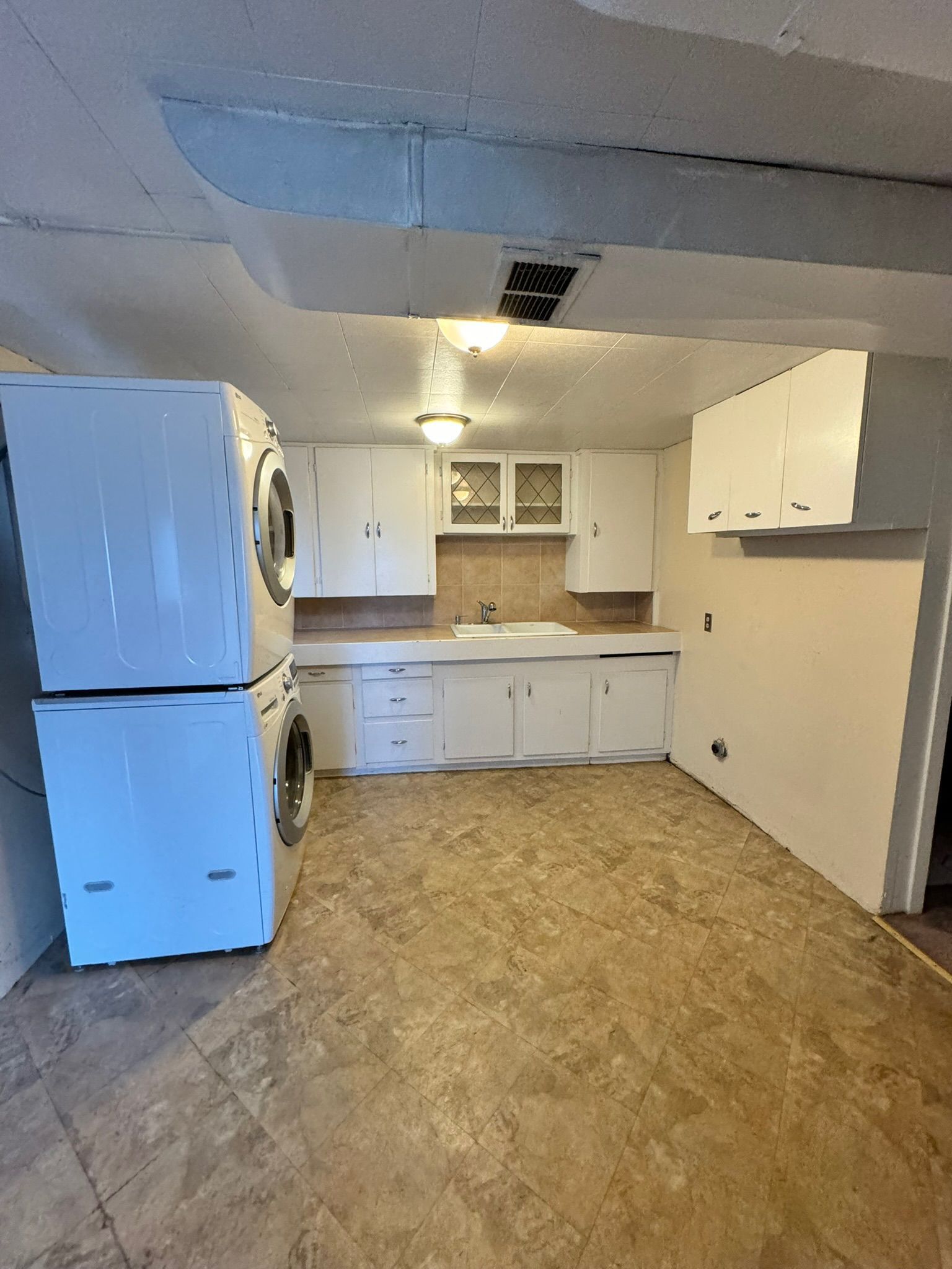 Small kitchen with white cabinets, refrigerator, and wood-patterned floor under a low ceiling.
