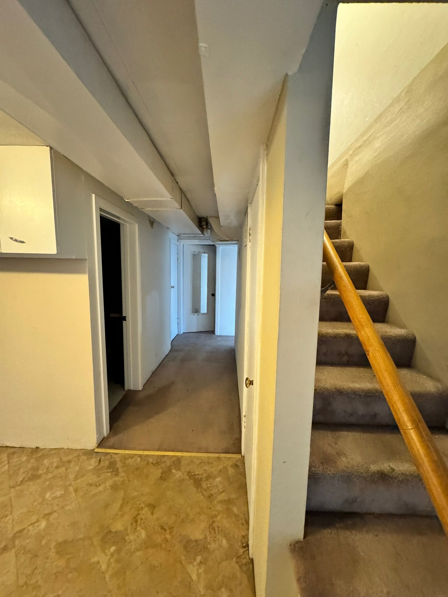 Narrow hallway with carpeted stairs on the right and doorways leading to a bright room at the end