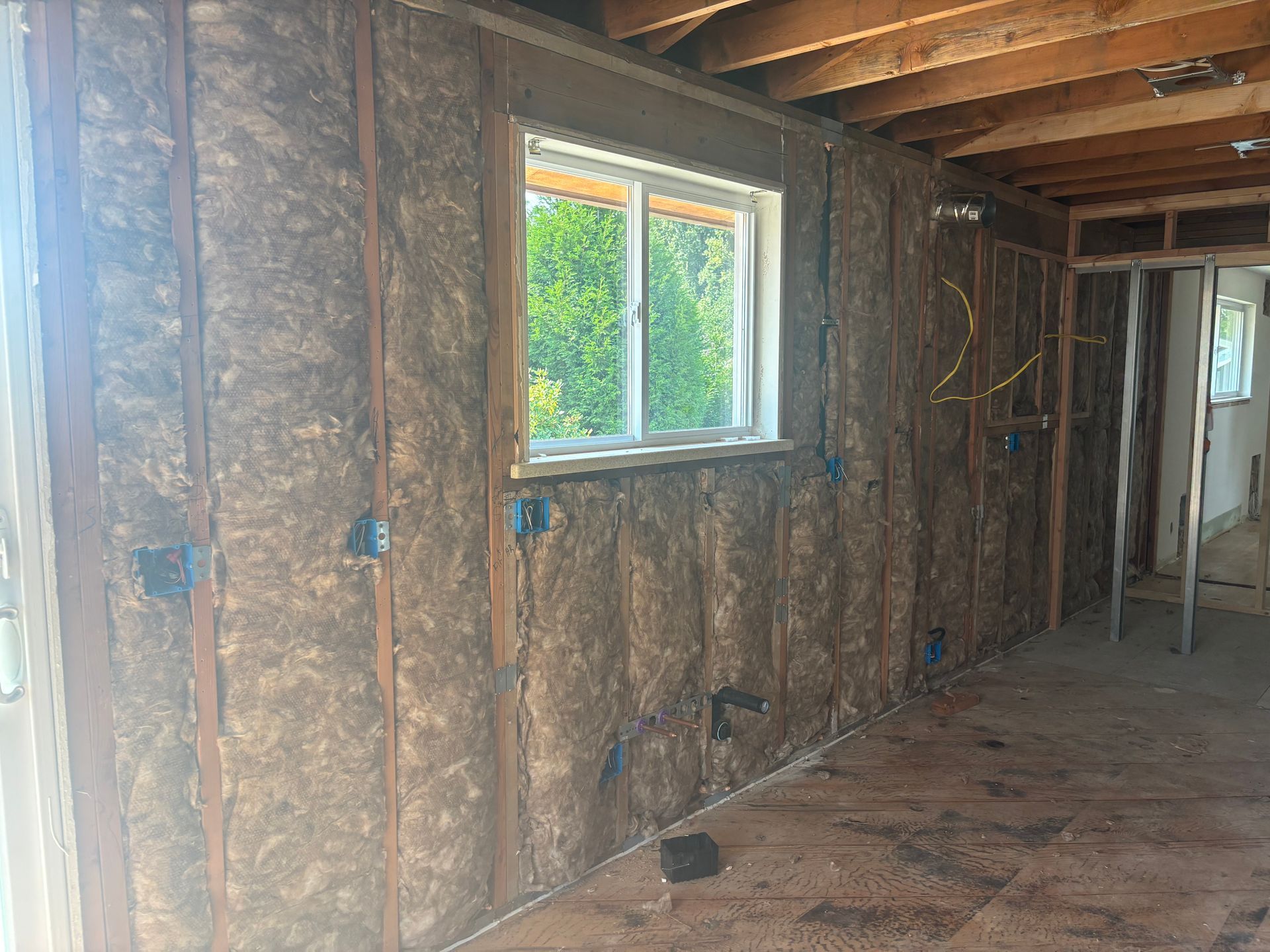 Unfinished room with exposed insulation, wooden beams, and a small window letting in daylight.
