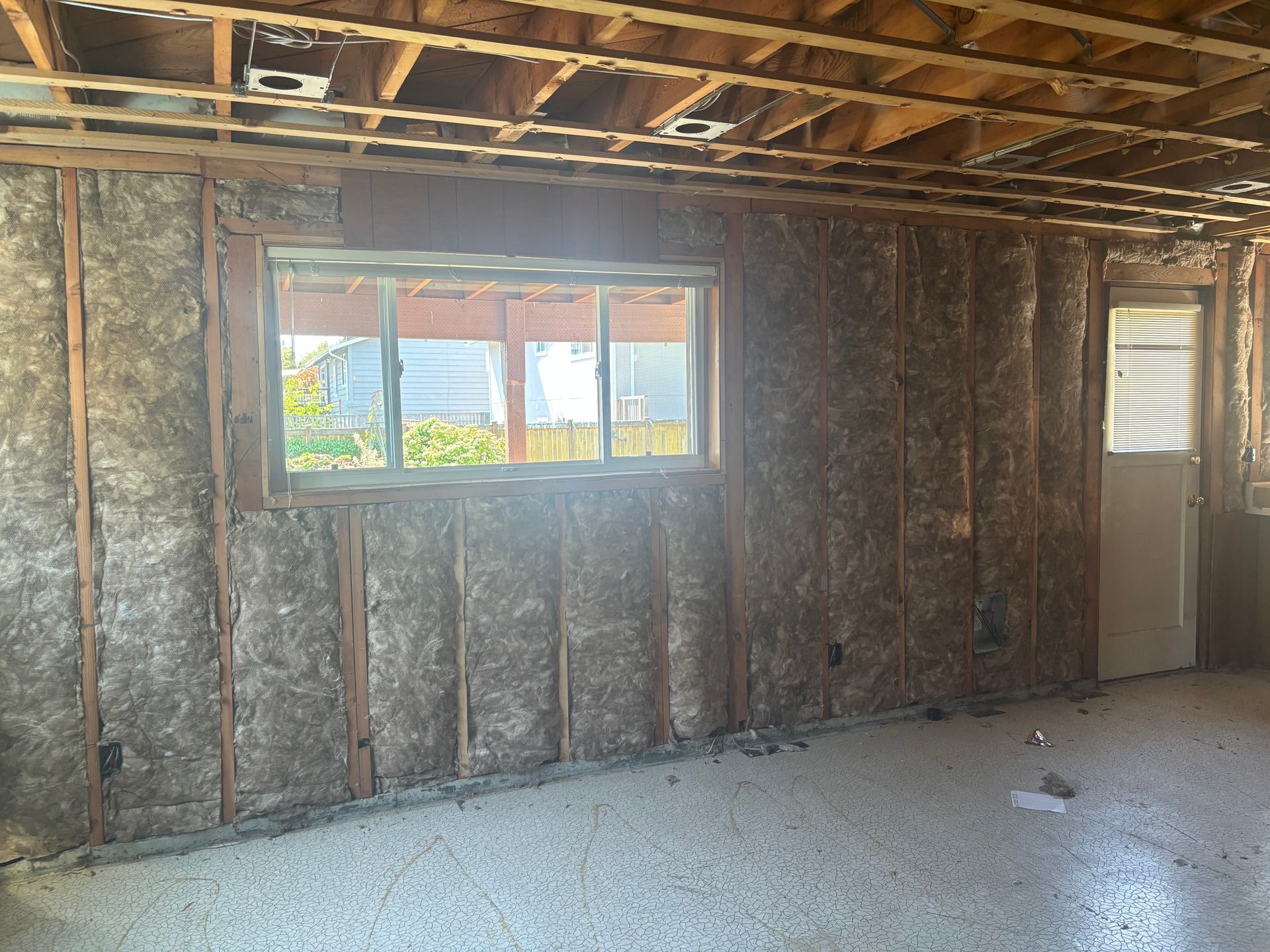 Unfinished room with exposed insulation, a window, and a door, with a bare concrete floor.