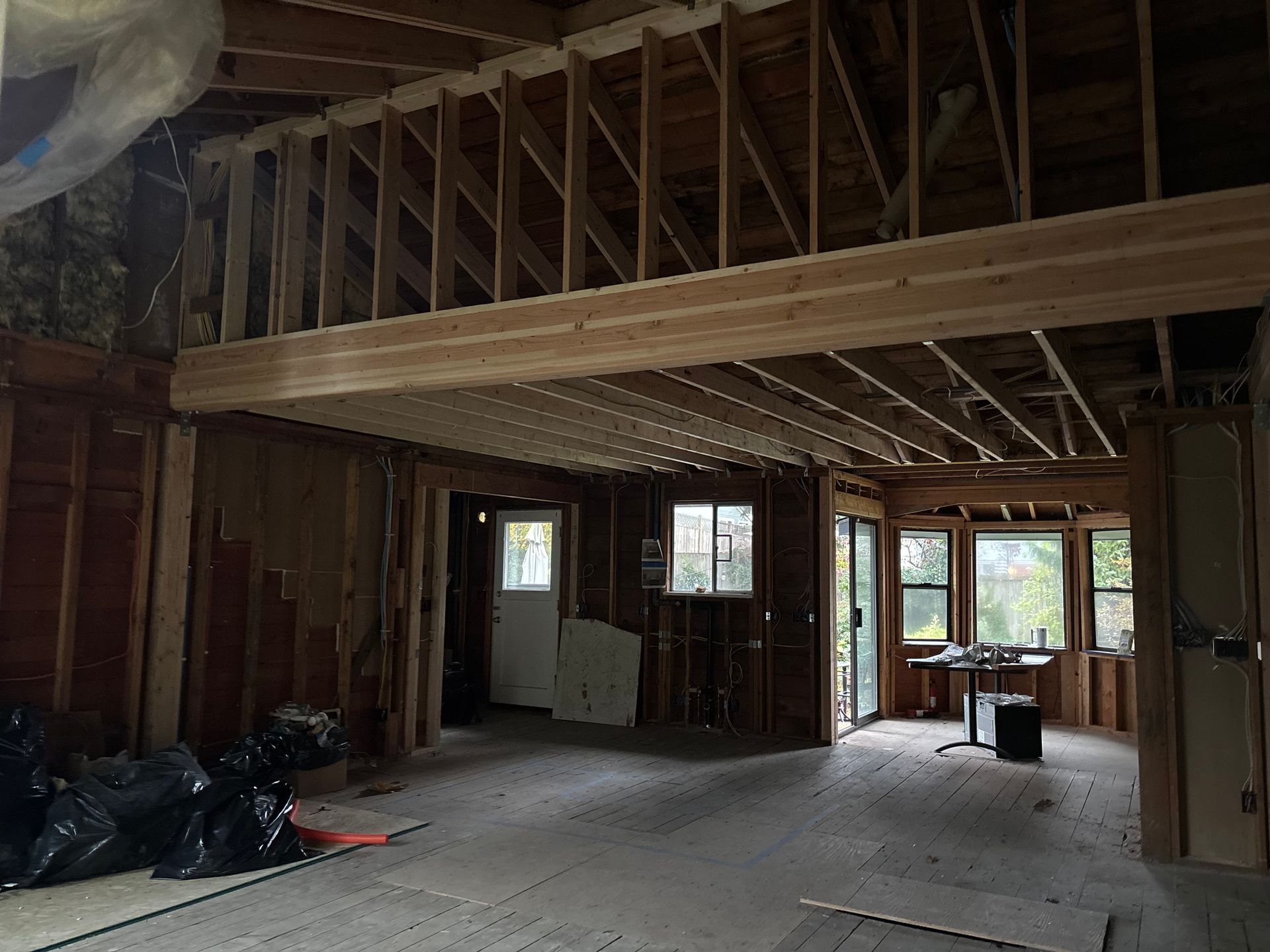 Unfinished room with exposed wooden framing, loft beams, windows, and construction debris on the floor